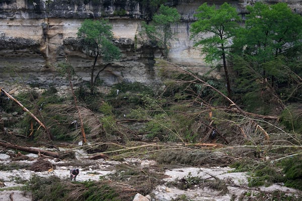 A Texas Department of Public Safety official, bottom left, combs through the banks of the Guadalupe River near Camp Mystic after a flash flood swept through the area Saturday, July 5, 2025, in Hunt, Texas. (AP Photo/Julio Cortez)