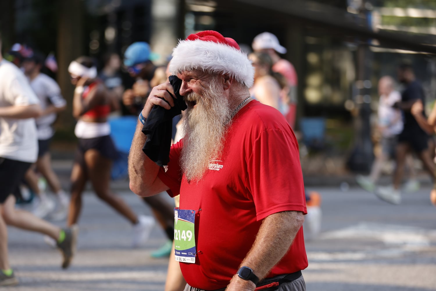 Runner in Santa hat wipes face in the heat at  the 56th running of the Atlanta Journal-Constitution Peachtree Road Race in Atlanta on Friday, July 4, 2025.   (Natrice Miller / AJC)