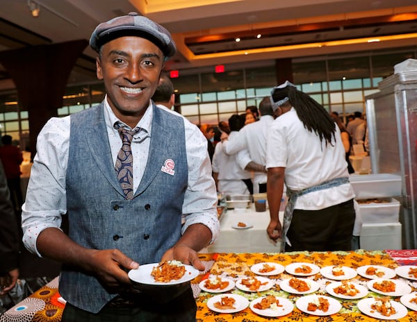 FILE - Chef Marcus Samuelsson, who is Ethiopian, but was raised in Sweden, founder of Red Rooster Harlem and more than a dozen other restaurants, holds a tasting plate of Dorowat "lasagna," with injera (Ethiopian flatbread), ayib (Ethiopian cheese), rosemary, and crispy skin, during the C-CAP (Careers through Culinary Arts Program) annual benefit, Feb. 27, 2018, in New York. (AP Photo/Kathy Willens, File)