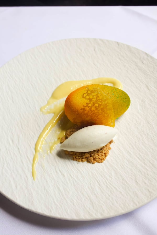Quenelles of mango mousse and Champagne sorbets are artfully garnished and arranged on a textured plate.