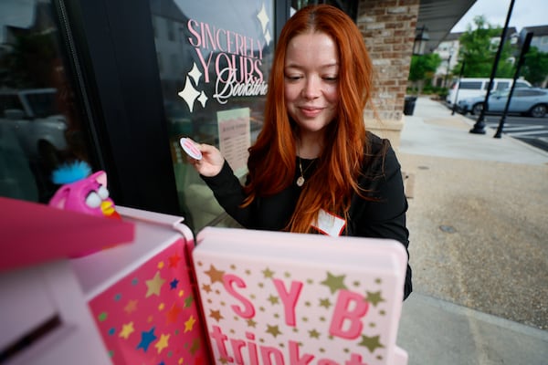 Destiny Sessums (29) of Fulton County happily secures a Dolly Parton pin after exchanging it for a whistle at the newly installed trinket box outside the Sincerely Yours bookstore on Wednesday, April 29, 2026.   (Miguel Martinez/AJC)