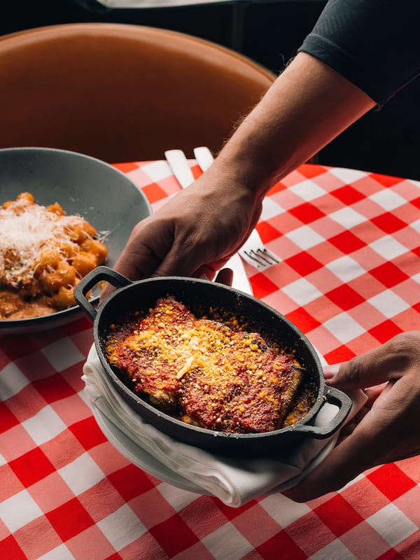 A dish of eggplant rollatini held above a checkered tablecloth