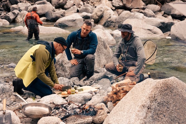 This image released by National Geographic shows Stanley Tucci, left, preparing a dish for anglers on the banks of the Sarca River during a visit to Italy's northernmost region, during the filming of his series "Tucci in Italy." (Matt Holyoak/National Geographic via AP)