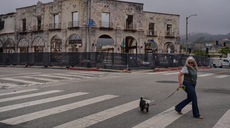 D. Berryman walks her dog, Tiny Dancer, past a fire-damaged building more than a year after the Palisades Fire in the Pacific Palisades neighborhood of Los Angeles, Thursday, June 4, 2026. (AP Photo/Jae C. Hong)