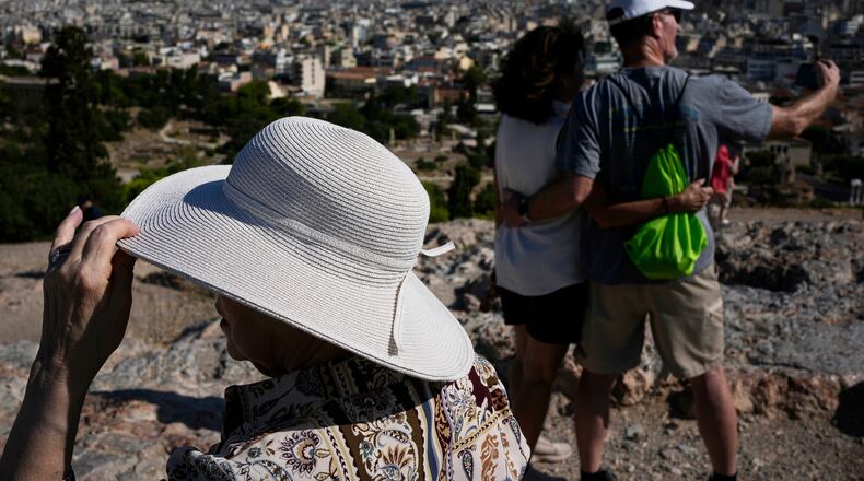 Tourists wearing hats take photographs on the rocky Areios Pagos Hill next to the Acropolis in Athens, Greece, Friday, Aug. 14, 2026. (AP Photo/Thanassis Stavrakis)