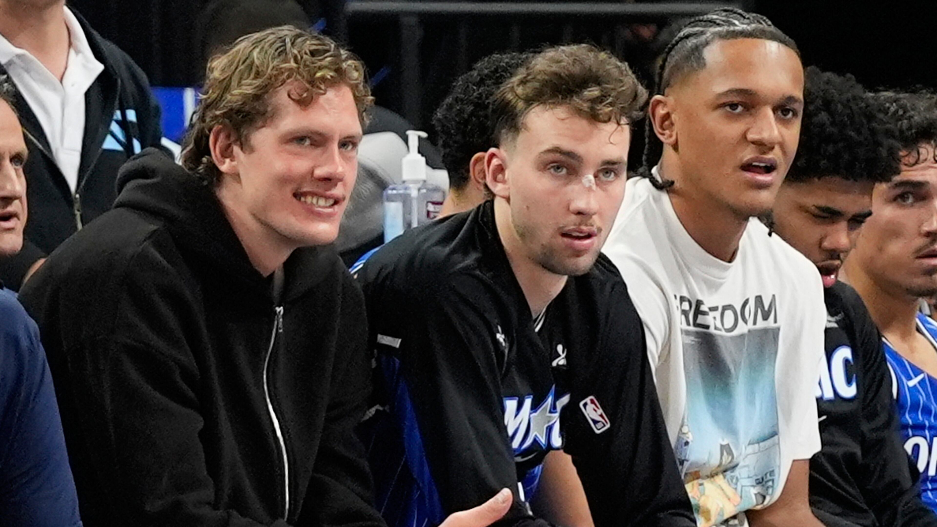 **HOLD FOR STORY BY ROB MADDIE**Orlando Magic players and brothers Moritz Wagner, left, and Franz Wagner, center, watch the first half of an NBA basketball game with teammate Paolo Banchero against the Golden State Warriors, Tuesday, Nov. 18, 2025, in Orlando, Fla. (AP Photo/John Raoux)