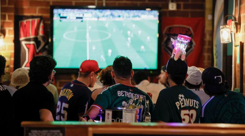 A group of customers, some wearing Mexico jerseys, watch a World Cup game on screens at Woofs Sport Bar in Midtown on Sunday, July 5, 2026. Woofs is the official location for Pride House ATL, the city’s designated hub for LGBTQ+ soccer fans during the FIFA World Cup. (Miguel Martinez/AJC)