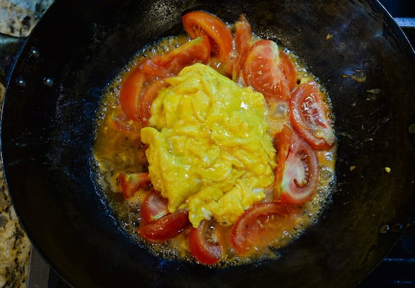 A close-up shot of the wok cooking the eggs, chicken broth mixture and tomatoes.