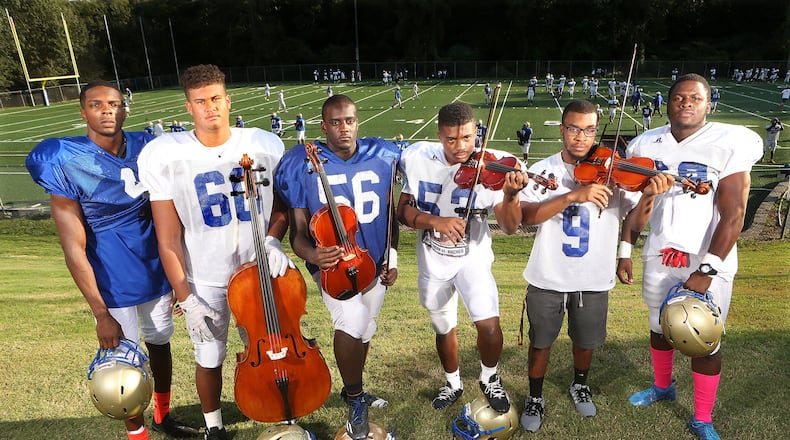 Cobb County’s McEachern High School football team has multiple skills. Wearing their practice jerseys are E.J. Scott (from left), Michael Fairbanks, Jeffrey Bryant, Dante Fleming, Justin Powell and Courtney Mills, who also play violin, viola and cello in the school orchestra. CURTIS COMPTON /CCOMPTON@AJC.COM