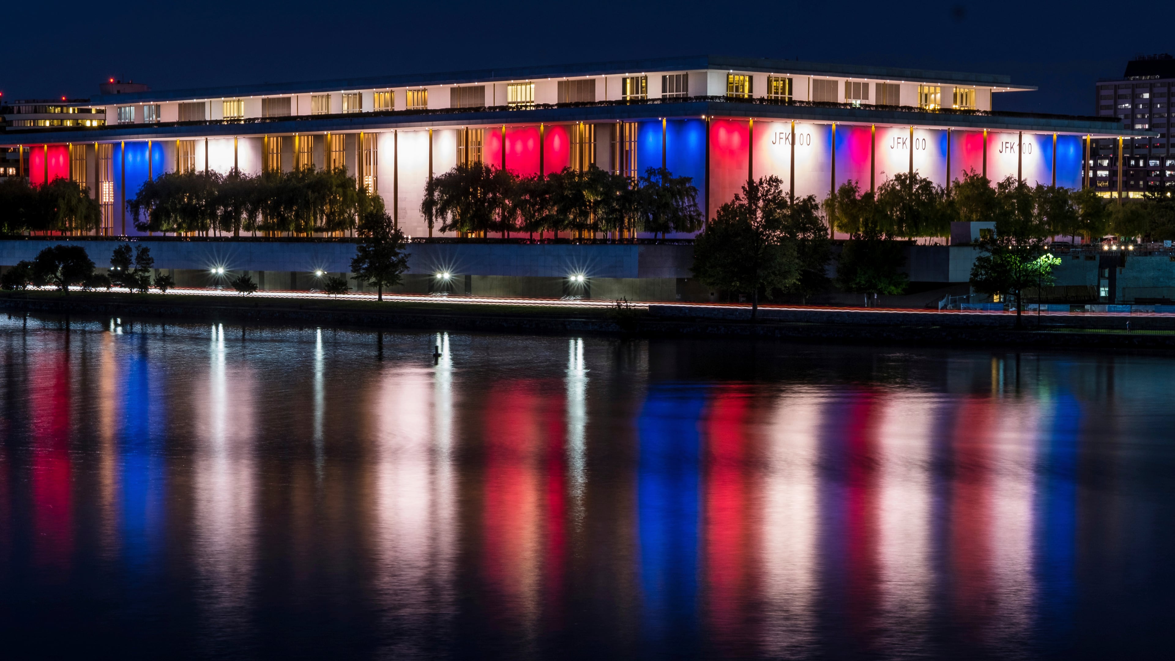 FILE - The red, white and blue lights, marking the 100th birthday of President John F. Kennedy, on the outside of the Kennedy Center for the Performing Arts are reflected in the Potomac River in Washington, May 26, 2017. AP Photo/J. David Ake, File)
