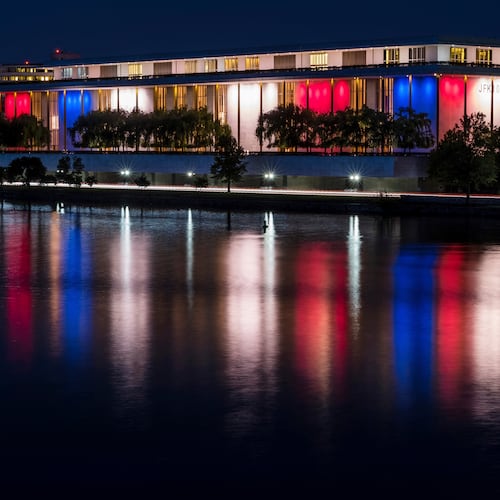 FILE - The red, white and blue lights, marking the 100th birthday of President John F. Kennedy, on the outside of the Kennedy Center for the Performing Arts are reflected in the Potomac River in Washington, May 26, 2017. AP Photo/J. David Ake, File)