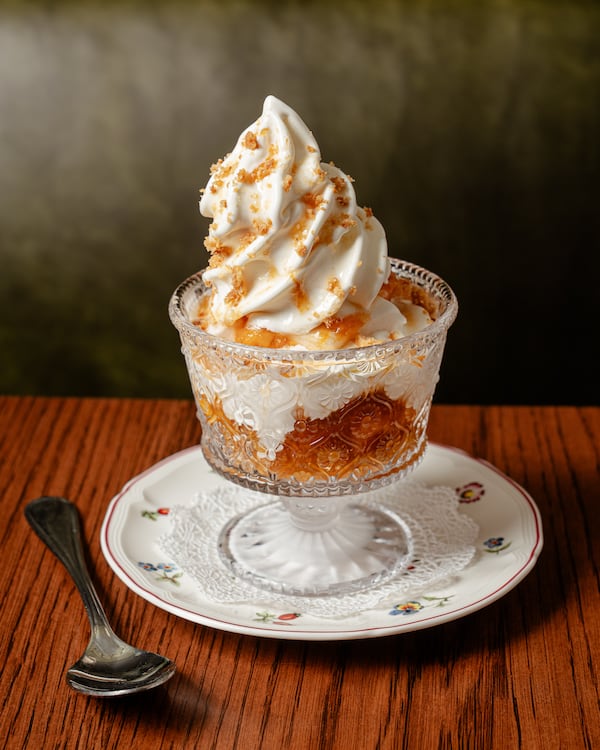 A sundae dish filled with peaches and a tall peak of soft-serve ice cream.