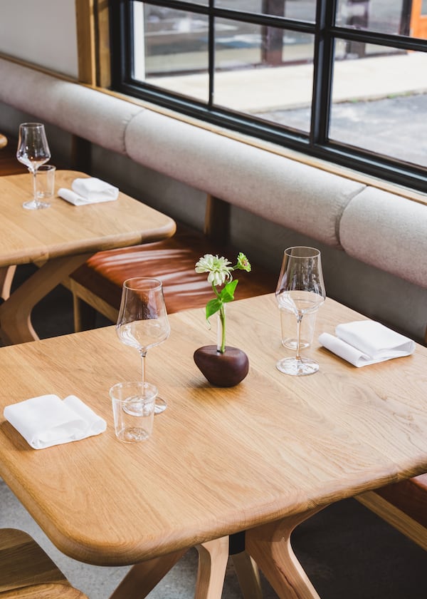 A blonde wood table with napkins and glassware for two, and a bud vase in the center.