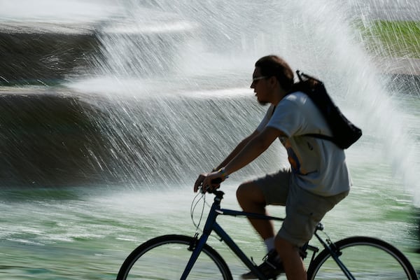 A cyclist rides past a fountain as temperatures approach 100 degrees, Friday, June 20, 2025, in Kansas City, Mo. (AP Photo/Charlie Riedel)