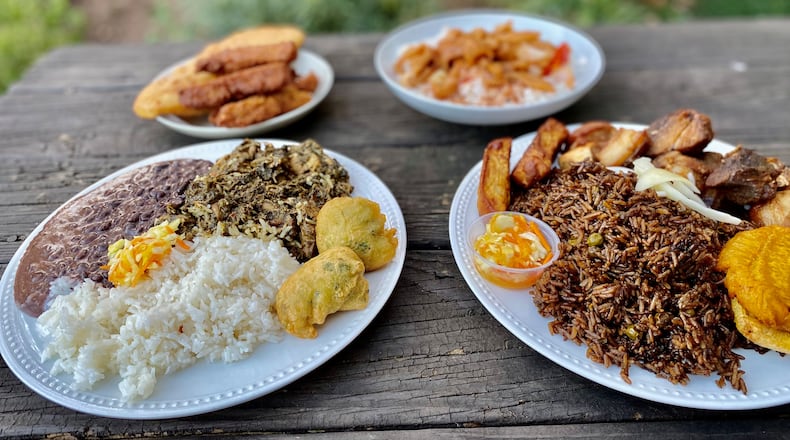 This takeout order from Jojo Fritay includes (left) lalo with white rice, black beans, pikliz and marinad; and (right) griot with fried plantains, mushroom rice, fried sweet potatoes and pikliz. In the background, a selection of fritay and conk stew. Wendell Brock for The AJC