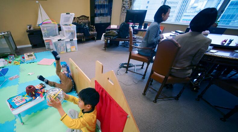 Keiko Kobayashi and Sachiko Aoki, both employees of the staffing services company Pasona Inc., work as their children entertain themselves at the company's headquarters Monday, March 2, 2020, in Tokyo. Many Japanese schools were shut down Monday and spring holidays began unexpectedly early for children as part of a government-led measure to prevent further escalation of the coronavirus. (AP Photo/Eugene Hoshiko)