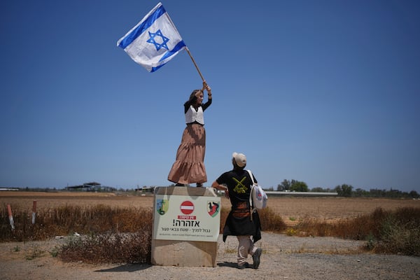 An activist stands on a concrete block signaling border ahead as she waves an Israeli flag towards trucks loaded with humanitarian aid for the Gaza Strip in southern Israel, Wednesday, May 21, 2025. (AP Photo/Ohad Zwigenberg)