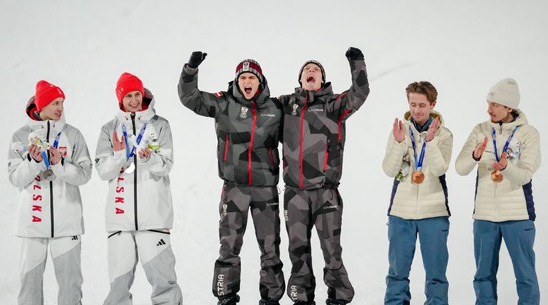 Gold medalists Stephan Embacher and Jan Hoerl, of Austria, celebrate on the podium, with silver medalists Pawel Wasek and Kacper Tomasiak, of Poland, and bronze medalists Kristoffer Eriksen Sundal and Johann Andre Forfang, of Norway, after the ski jumping men's super team competition at the 2026 Winter Olympics, in Predazzo, Italy, Monday, Feb. 16, 2026. (AP Photo/Matthias Schrader)