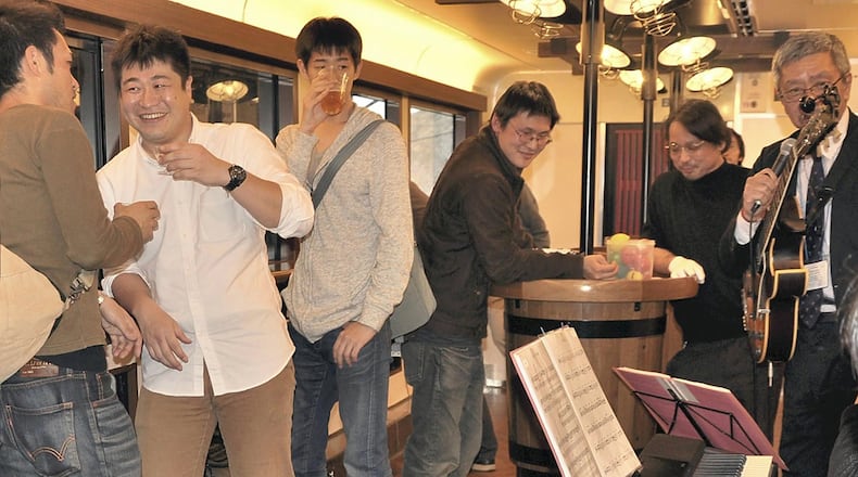 Reporter Masanori Matsumoto, second from left, samples the sake while listening to a live jazz performance on the Koshino Shu Kura train. The table is designed to resemble a sake barrel. PHOTO: Japan News-Yomiuri