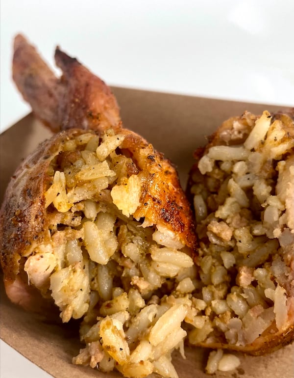 A close-up shot of a chicken wing opened to show boudin stuffing, including seasoned rice, spilling out.
