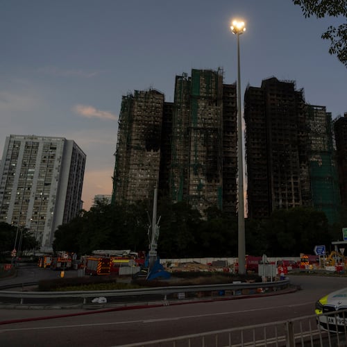 A man walks past charred buildings burnt after a deadly fire that started Wednesday at Wang Fuk Court, a residential estate in the Tai Po district of Hong Kong's New Territories, Friday, Nov. 28, 2025. (AP Photo/Ng Han Guan)