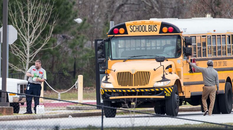 A Fulton County Public Schools employee (left) handles a bottle of commercial disinfectant in the parking lot at Woodland Middle School in East Point, Monday, March 9, 2020. (ALYSSA POINTER/ALYSSA.POINTER@AJC.COM)