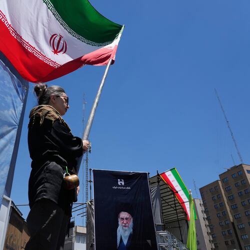 A woman waves an Iranian flag during a pro-government campaign as a portrait of the slain Supreme Leader Ayatollah Ali Khamenei, who was killed in U.S. and Israeli strikes on Feb. 28, is displayed at right, in downtown Tehran, Iran, Monday, June 15, 2026. (AP Photo/Vahid Salemi)