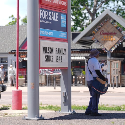 As the daytime high temperature soars into the 80s, a United States Postal Service postman keeps cool by standing in the shade of a gasoline station sign posting the per-gallon prices for the various grades of fuel available Thursday, June 4, 2026, in central Denver. (AP Photo/David Zalubowski)