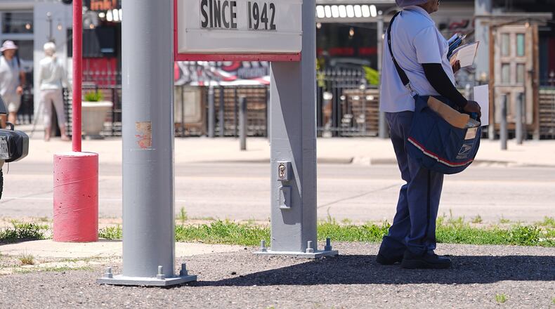 As the daytime high temperature soars into the 80s, a United States Postal Service postman keeps cool by standing in the shade of a gasoline station sign posting the per-gallon prices for the various grades of fuel available Thursday, June 4, 2026, in central Denver. (AP Photo/David Zalubowski)