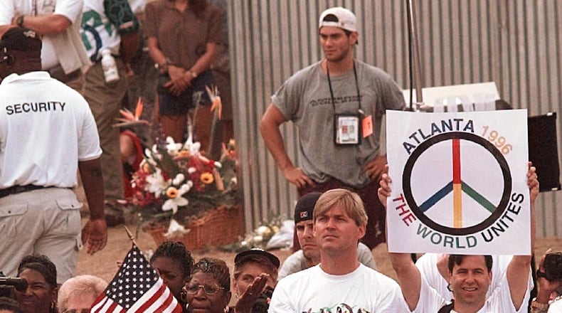 With a bouquet of flowers (background) marking the point of detonation of Saturday's fatal bombing, Olympic fans gather for a memorial ceremony at the reopening of Centennial Park at the Centennial Summer Olympics in Atlanta on Tuesday, July 30, 1996. (AP Photo/John Gaps III)