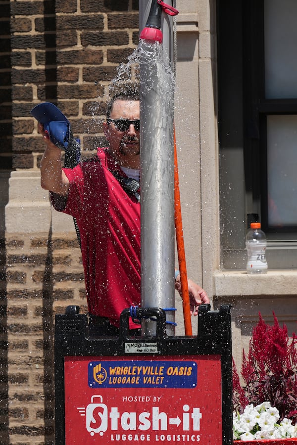 A Chicago Cubs security guard cools off under a sprinkler provided by a Chicago Fire Department outside of Wrigley Field before a baseball game between the Seattle Mariners and the Chicago Cubs in Chicago, Sunday, June 22, 2025. (AP Photo/Nam Y. Huh)