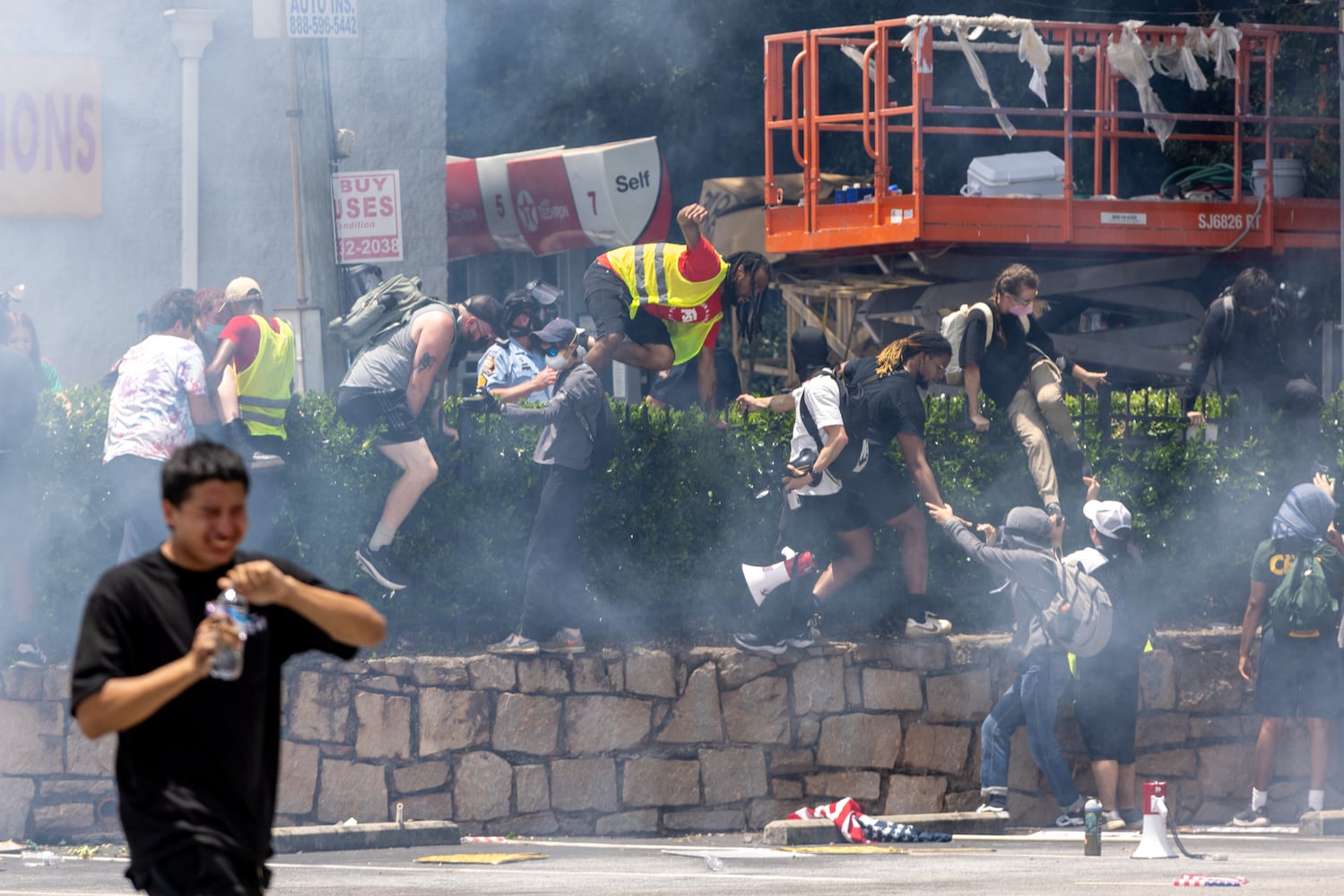 Demonstrators climb a hedge to avoid tear gas during a protest on ICE raids and deportation arrests on Chamblee Tucker Road in Atlanta on Saturday, June 14, 2025. (Arvin Temkar / AJC)
