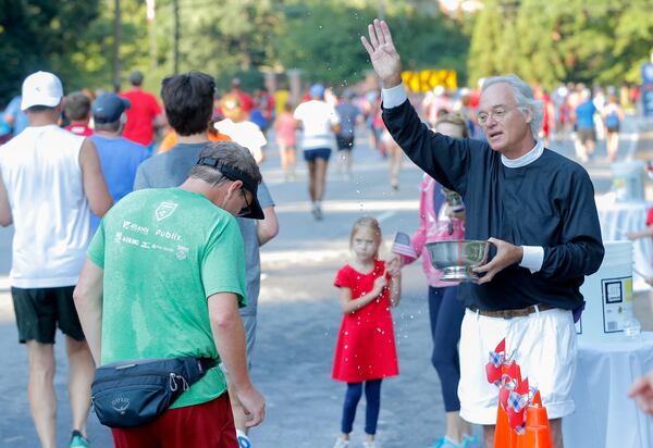 Sam Candler, an Episcopal priest, blesses a runner outside the Cathedral of St. Philip during the AJC Peachtree Road Race on Sunday, July 4, 2021. (Christine Tannous/AJC)