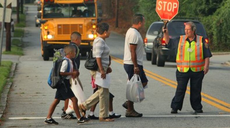 DeKalb, Atlanta and Gwinnett schools were among districts opening their doors to students on Monday. Faye Bishop, a 25-year DeKalb County police crossing guard, helps parents and children cross Curtis Drive near Woodward Elementary School.
