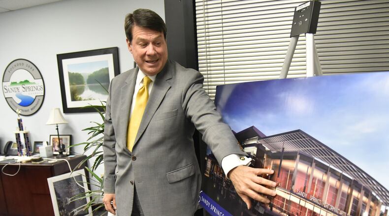 Rusty Paul, mayor of Sandy Springs, shows off concept photographs of new Sandy Springs City Center at his office. For years, the city of Sandy Springs was held up as a model for how to keep government efficient by outsourcing almost all services to private companies. Now, the young city of Stonecrest is looking to copy Sandy Springs, while South Fulton is launching with a more traditional government. HYOSUB SHIN / HSHIN@AJC.COM