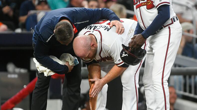 Braves catcher Brian McCann is tended to by trainer Mike Frostad, left, after being thrown out sliding into third base by Miami Marlins catcher Jorge Alfaro on a bunt by Kyle Wright during the fifth inning. (AP Photo/John Amis)