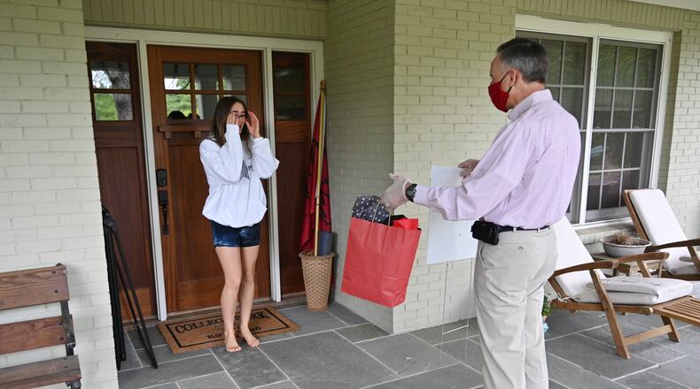 Izzy Wheeler, graduating senior, reacts as Dr. Stuart Gulley, president of Woodward Academy, personally delivers a special gift bag and yard sign at her home in College Park on Tuesday, April 28, 2020. The private school with campuses in College Park and Johns Creek, ended its school year that day, and teachers and staff personally delivered special treats and spirit wear to seniors’ houses. HYOSUB SHIN / HYOSUB.SHIN@AJC.COM