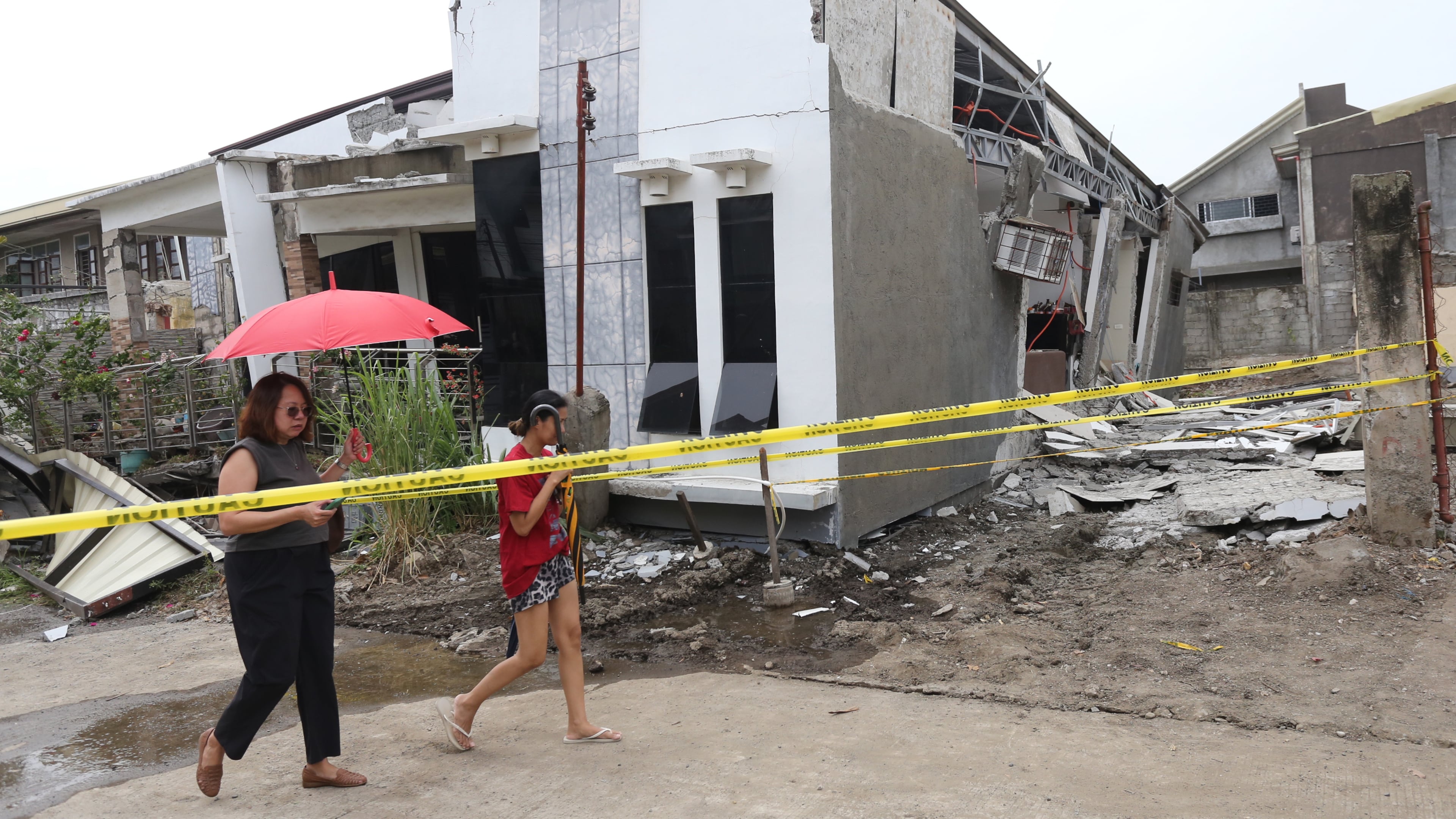 Two women walk past a damaged house after a strong earthquake in Davao City, southern Philippines on Friday Oct. 10, 2025. (AP Photo/Manman Dejeto)