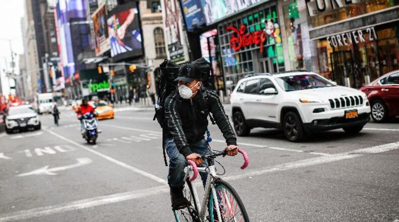 A bicycle delivery worker wears a protective face mask as he rides through a sparsely populated Times Square due to COVID-19 concerns, Friday, March 20, 2020, in New York. (AP Photo/John Minchillo)