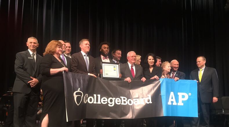 Gwinnett County and College Board officials hold a banner after the school district was named Advanced Placement District of the Year for its efforts to get more students to take AP courses and its improved performance. Duluth High School student Cameren Carter holds a plaque with details about the honor. ERIC STIRGUS/ESTIRGUS@AJC.COM