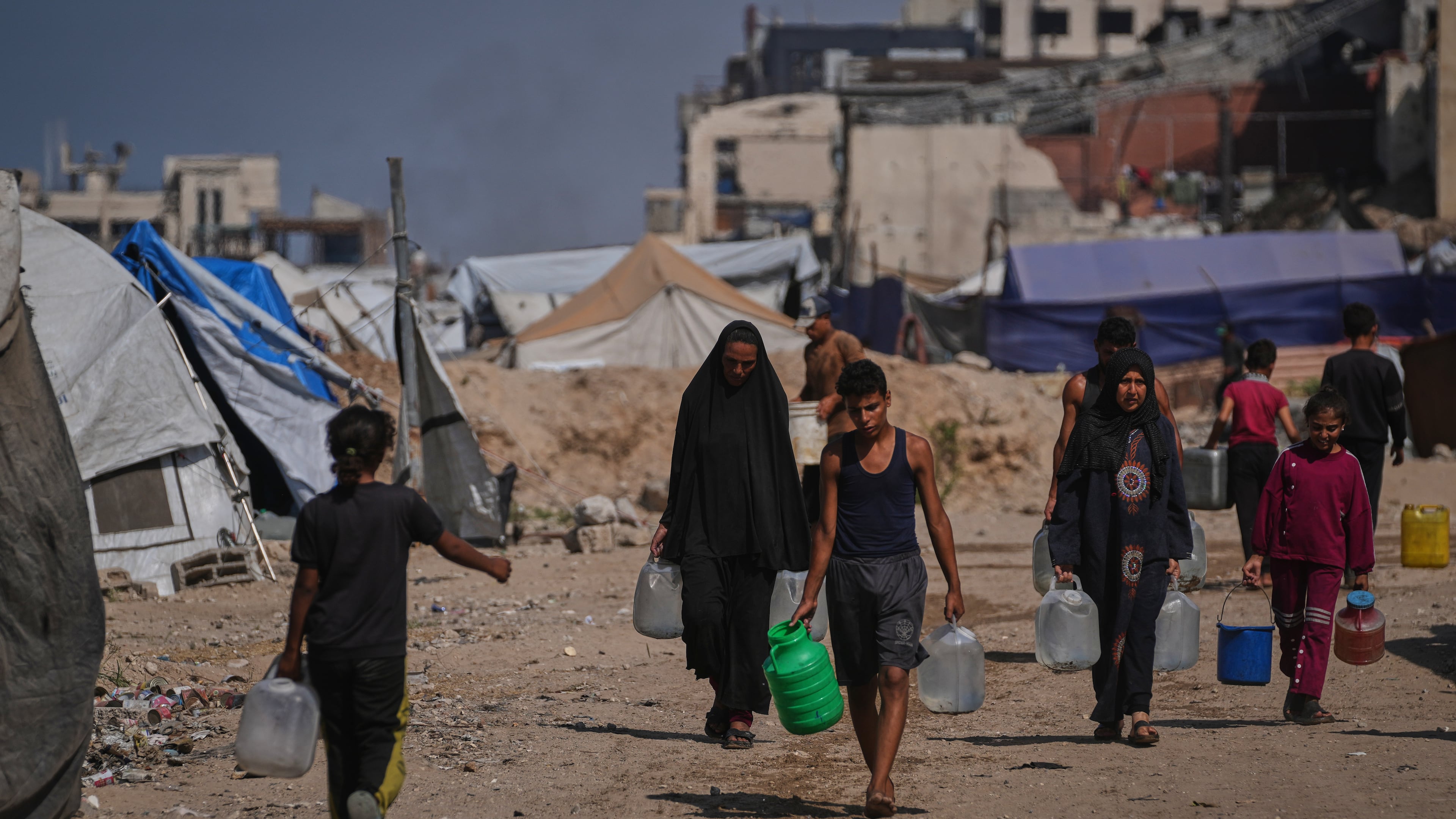 Palestinians carry jerrycans and plastic bottles with water after collecting it at a camp for displaced people in Gaza City, Thursday Oct. 23, 2025. (AP Photo/Abdel Kareem Hana)