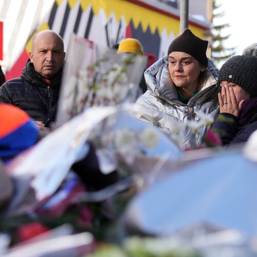 People mourn behind flowers and letters near the sealed off Le Constellation bar, where a devastating fire left dead and injured during the New Year's celebrations in Crans-Montana, Swiss Alps, Switzerland, Friday, Jan. 2, 2026. (AP Photo/ Antonio Calanni)