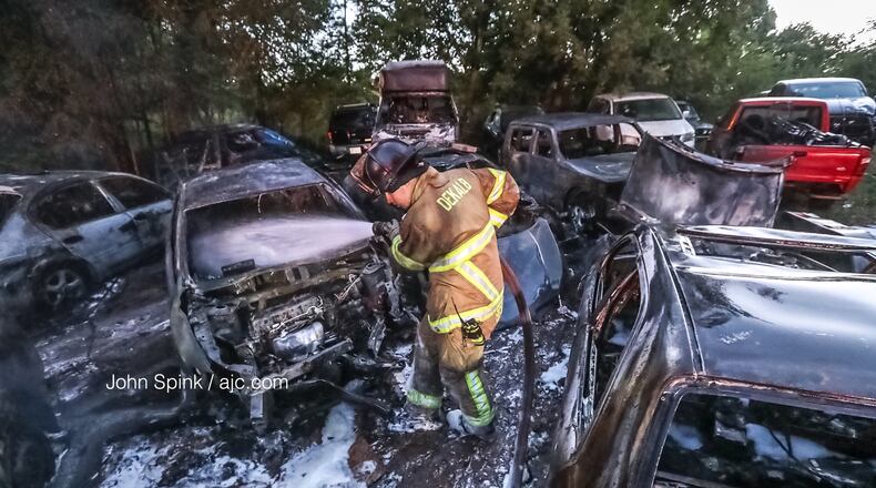 DeKalb County firefighter Joseph Brown works to put out a smoldering vehicle Friday morning, one of at least 12 that burned at a lot attached to an auto body shop north of Lithonia. Two more cars were found burning on Glenwood Road, but officials do not know if the two incidents are connected.