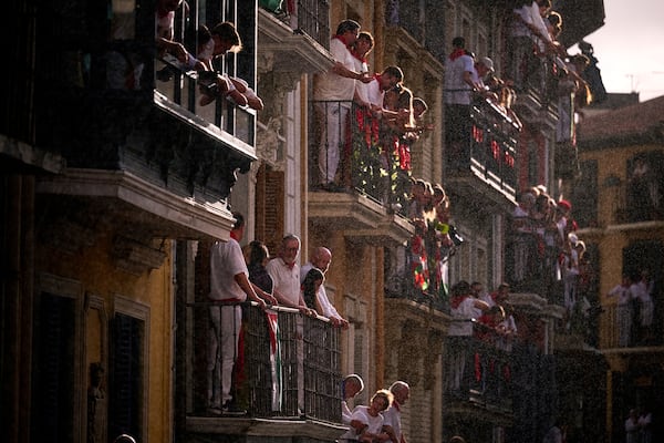 Attendees wait on their balconies as rain begins to fall during the first day of the running of the bulls, at the San Fermín fiestas in Pamplona, Spain, Monday, July 7, 2025. (AP Photo/Miguel Oses)