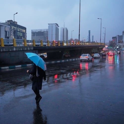 A woman holds an umbrella while crossing a street as rain falls in Tehran, Iran, Wednesday, Dec. 10, 2025. (AP Photo/Vahid Salemi)