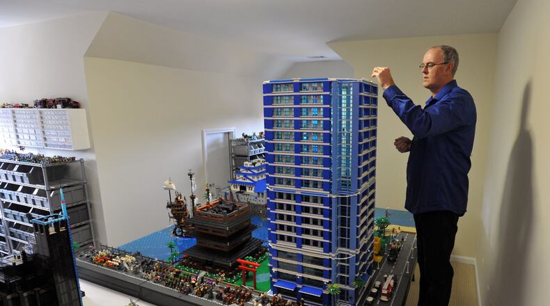 Harry Nijenkamp works on a small portion of the much larger city he and his son, Austin, are building. Only nine of the 25 total panels will fit into the special room in his home dedicated to Lego building. BRANT SANDERLIN / BSANDERLIN@AJC.COM
