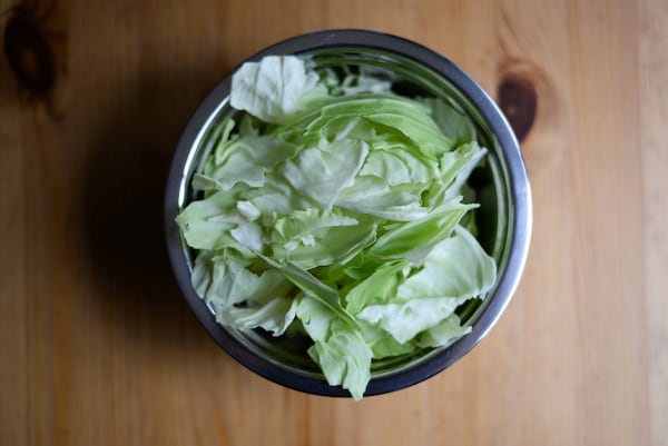 A bowl of torn cabbage leaves on a wooden table.