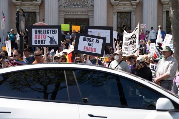 A Tesla vehicle drives past demonstrators during a rally against President Donald Trump and Tesla CEO Elon Musk in San Jose, Calif., on Saturday, April 5, 2025, as part of the nationwide "Hands Off!" protest. (AP Photo/Emily Steinberger)