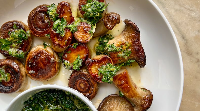 Dark golden brown seared king trumpet and white button mushrooms are topped with zesty lemon gremolata, with an additional bowl of the herby sauce on the side. (Virginia Willis for The Atlanta Journal-Constitution)