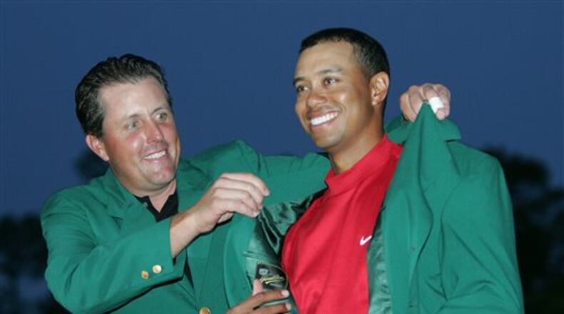 FILE - In this April 10, 2005, file photo, Tiger Woods, right, gets help with his green jacket from Phil Mickelson, left, after winning the Masters at Augusta National Golf Club in Augusta, Ga. The first tee on the opening day of the Masters might be the closest thing to a living, breathing interactive Hall of Fame exhibit in sports. Past Masters champions are invited to strike a ceremonial opening tee shot each year. Don't worry about a drop-off in quality anytime soon, either. Still in the pipeline are Tom Watson, Nick Faldo, Mickelson and Woods.(AP Photo/Morry Gash, File)